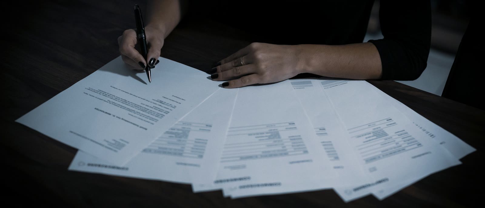 A business owner signing documents spread across a dark table