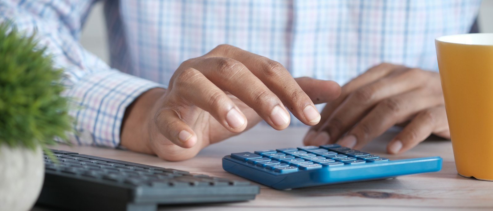 Hands working a calculator at a desk next to a coffee mug